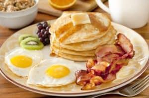 Pancakes, eggs, bacon, and fruit on a plate.