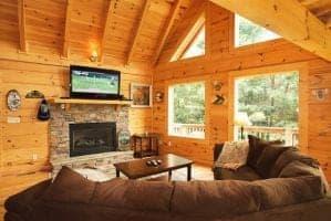 Living room of log cabin with large windows and stone fireplace